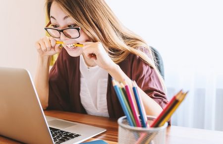 asiatische Frau vor Laptop beisst in einen Bleistift