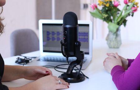 Mikro auf dem Tisch vor Laptop, davor sitzen zwei Frauen