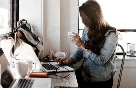 Frau sitzt mit Laptop und Tasse in der Hand im Profil vor dem Fenster, 