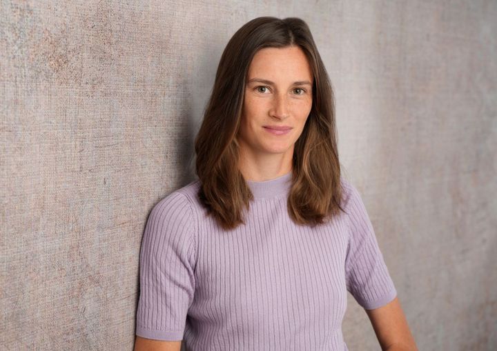 Eine Frau mit fliederfarbenem Oberteil schaut freundlich in die Kamera.