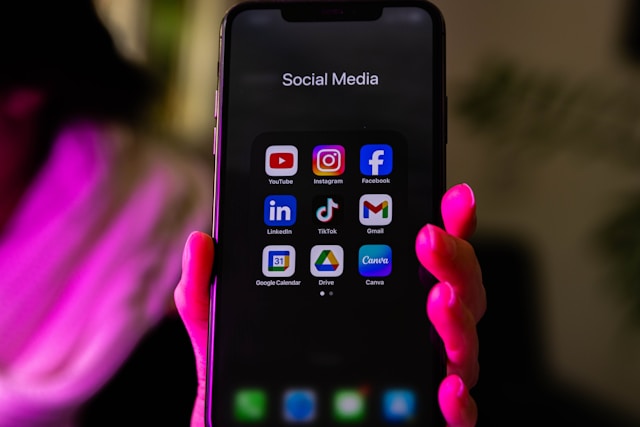 dlxmedia/ unsplash Frauenhand hält Handy mit Social Media Icons, rötliches Licht
